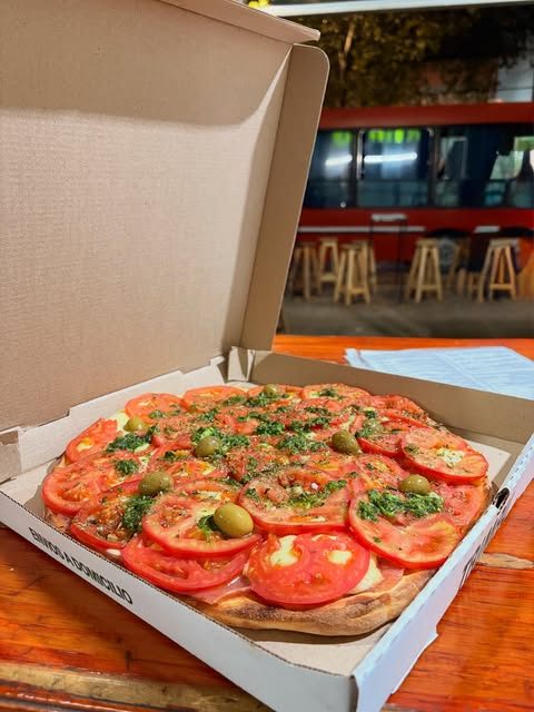 Pizza con rodajas de tomate en su caja de envío a domicilio